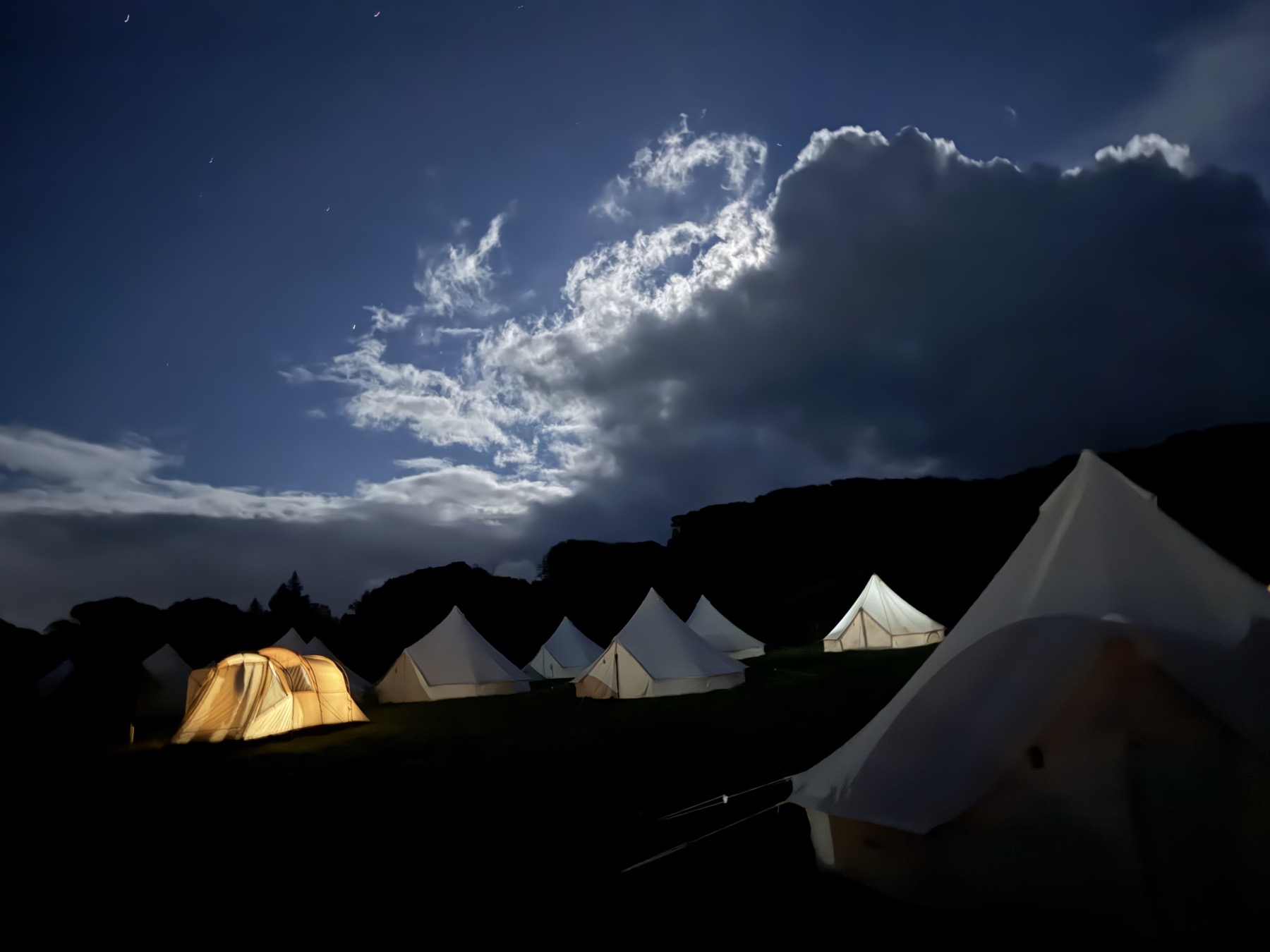 Bell tents lit up under a moonlit sky on the last night of Krankenhaus Festival 2026